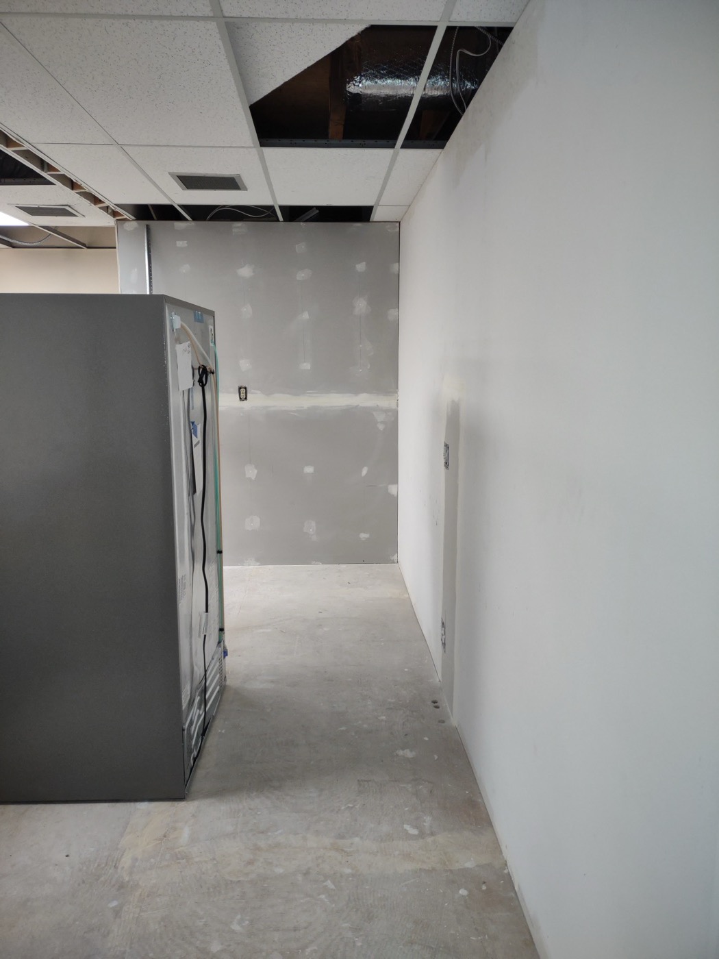 Primed and finished walls in a commercial remodel with stainless refrigerator visible